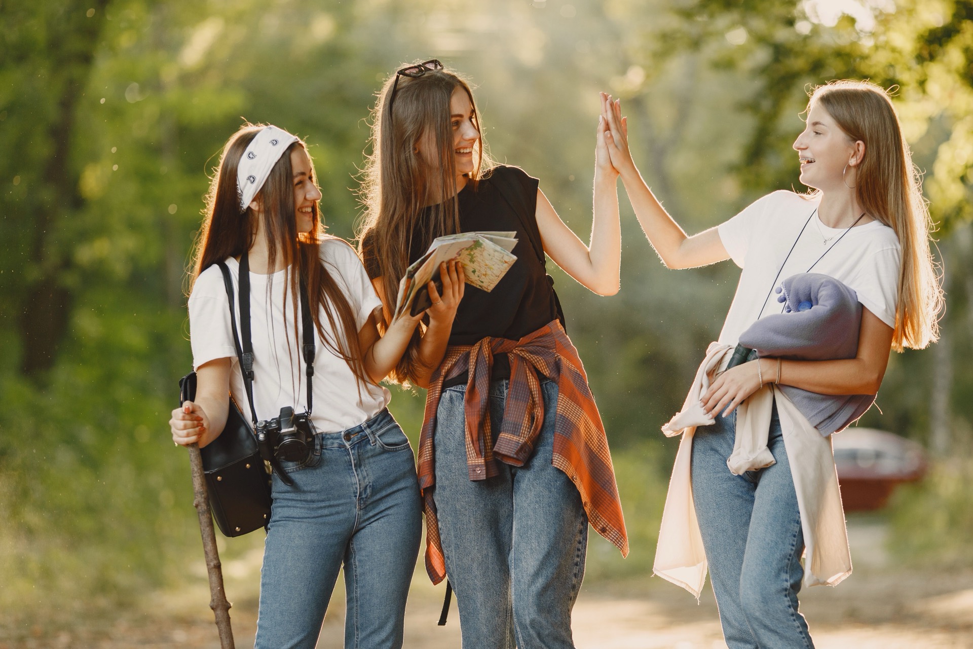 Three teenage girls laughing and high-fiving on a sunlit forest path
